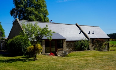 Gable Cottage under blue skies, surrounded by open lawn and trees at Mossyards