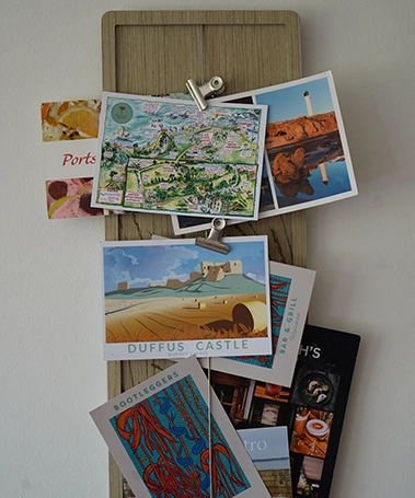 Wall-mounted pinboard displaying postcards, maps, and local restaurant cards